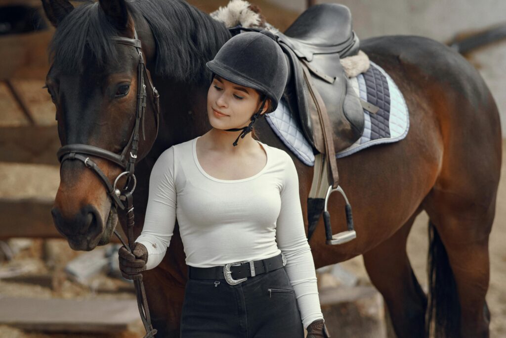 A young woman in equestrian gear stands with a horse, showcasing a serene bond.
